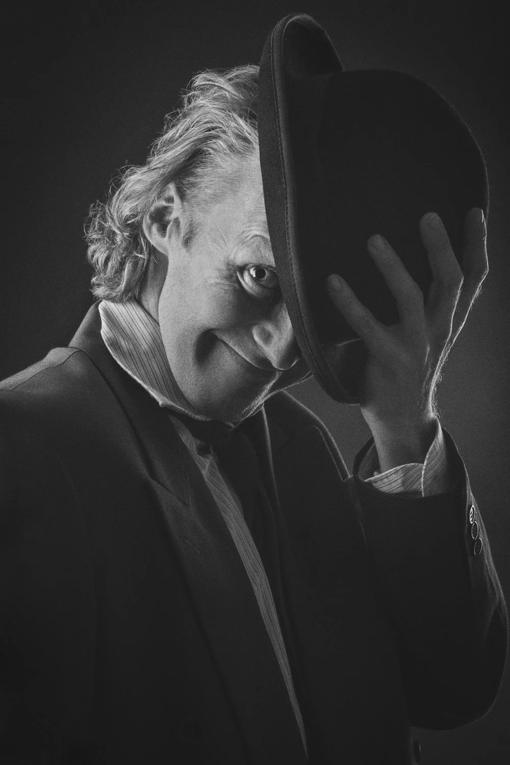 Ritratto in studio in bianco e nero dell'attore Cathal Carroll che solleva una bombetta davanti al volto, lasciando visibile un solo occhio in penombra