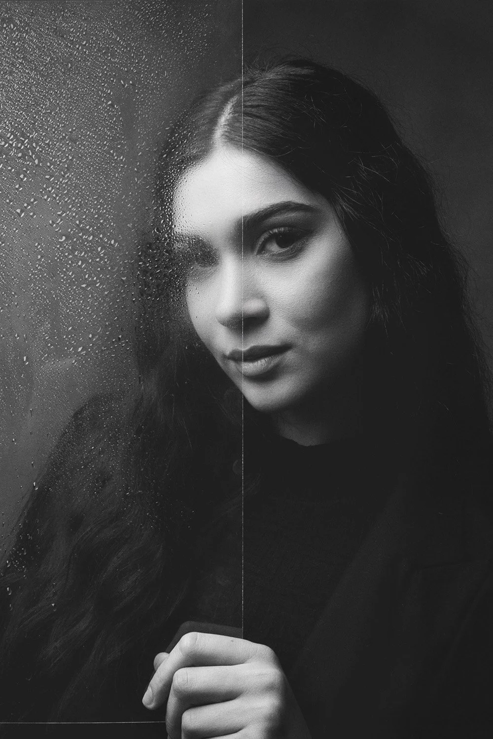 Ritratto in bianco e nero di una donna che tiene una lastra di vetro con gocce d'acqua. Un lato del viso è nitido, l'altro è filtrato dal vetro.