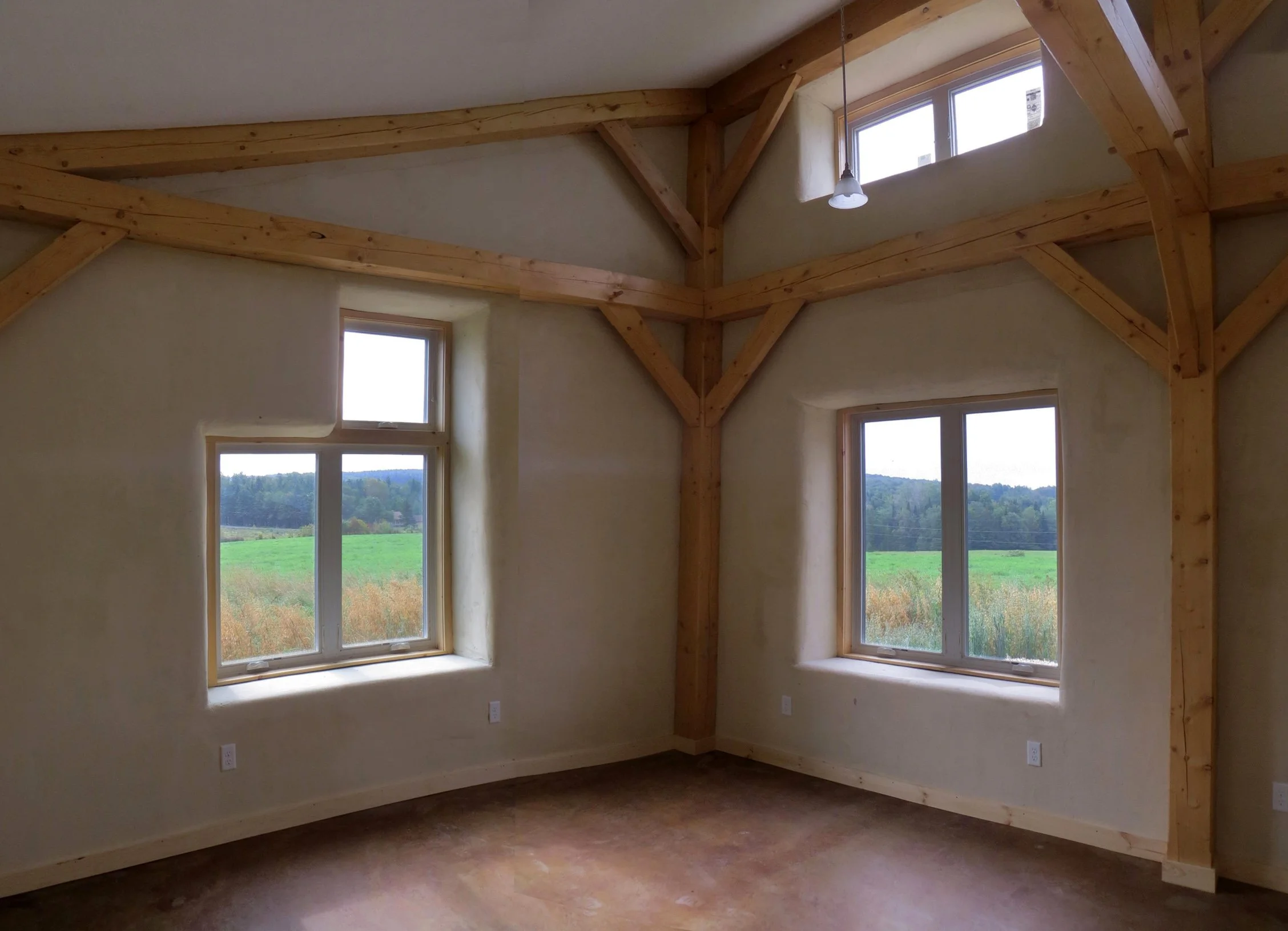Living area interior view to southeast. Shows polished concrete floor, post and beam along with finished strawbale walls. By Arocordis Design.