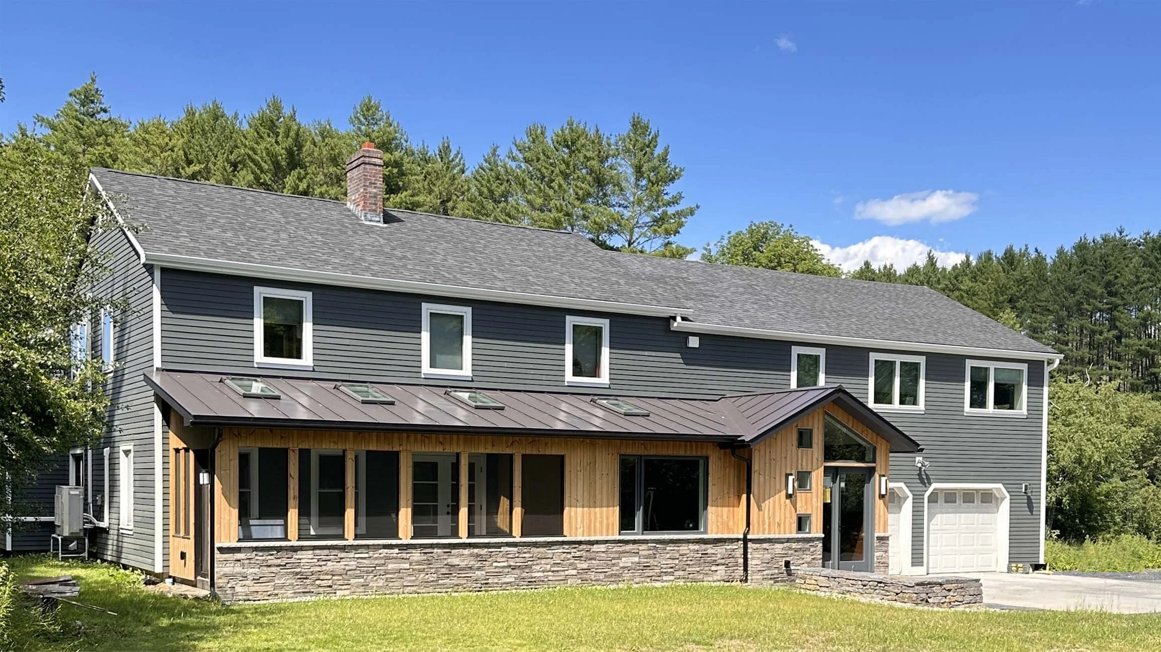 Modern front entry addition and screened porch on a renovated home in Montpelier, VT by Arocordis Design, featuring dark grey Hardie siding, warm wood accents, natural stone veneer, and skylights.