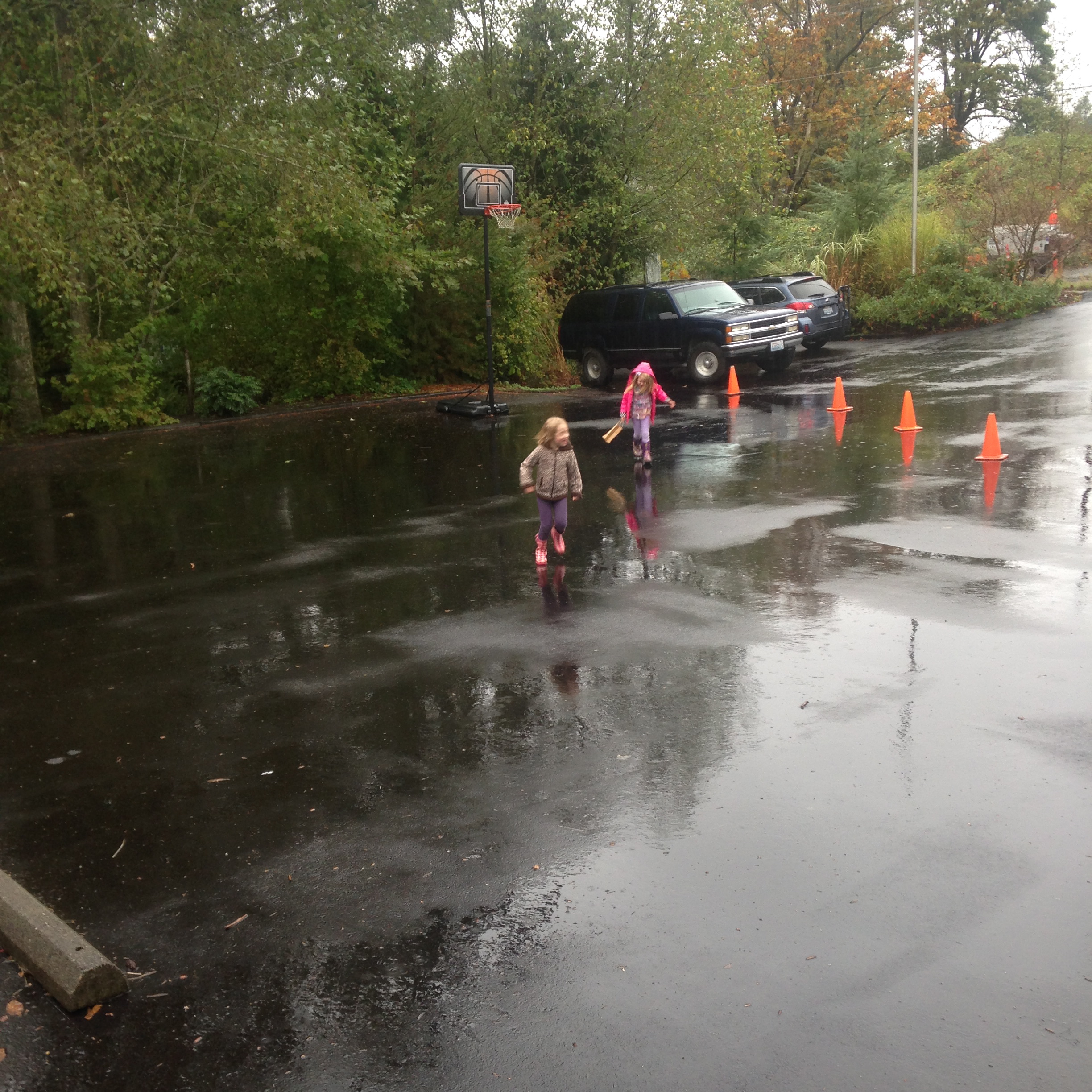 Two young students playing in puddles in a blocked off section of the parking lot.