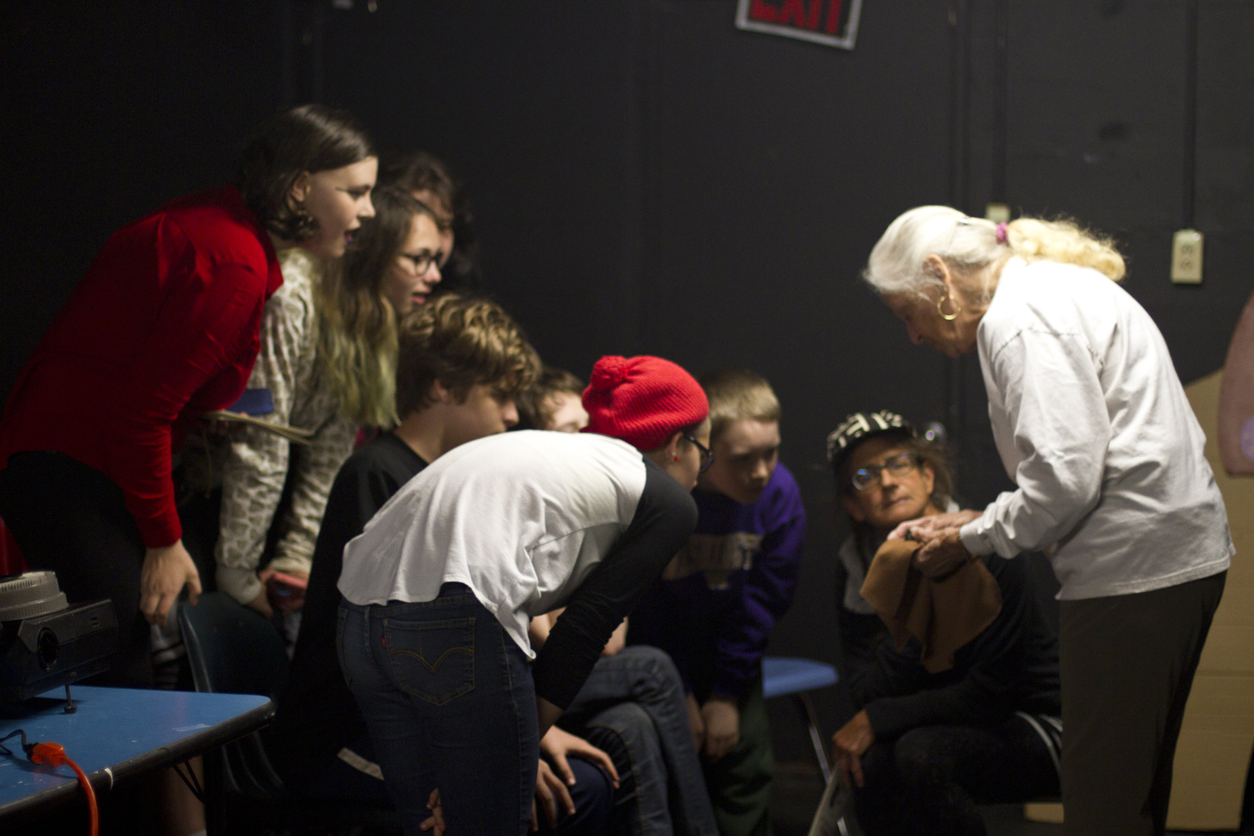 Group of students crowding around an older adult who is displaying something in their hands during a presentation on bats.