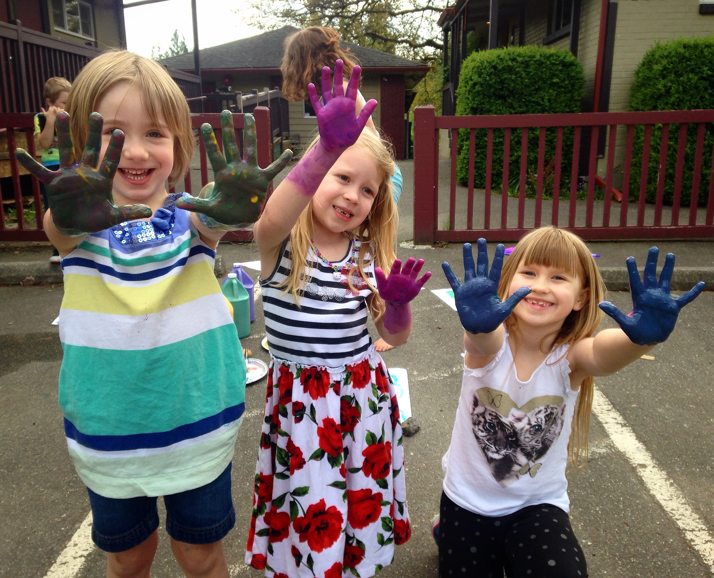 Three students display their paint-covered hands to the camera.