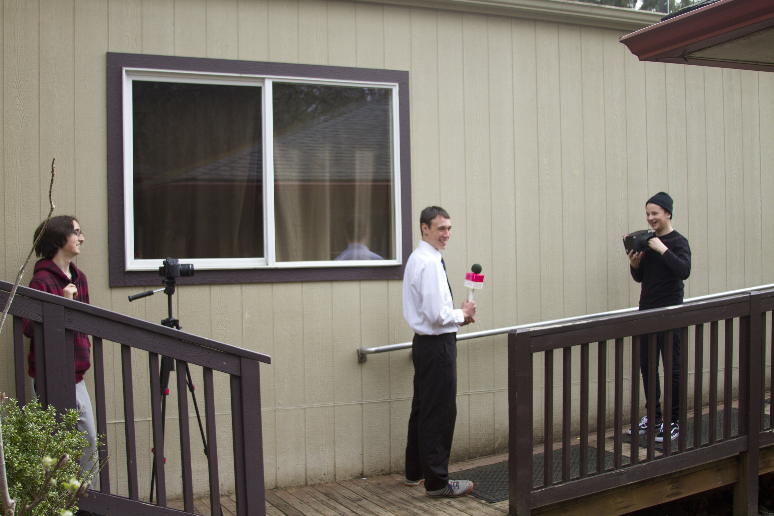 Two students filming another student, who holds a prop microphone.