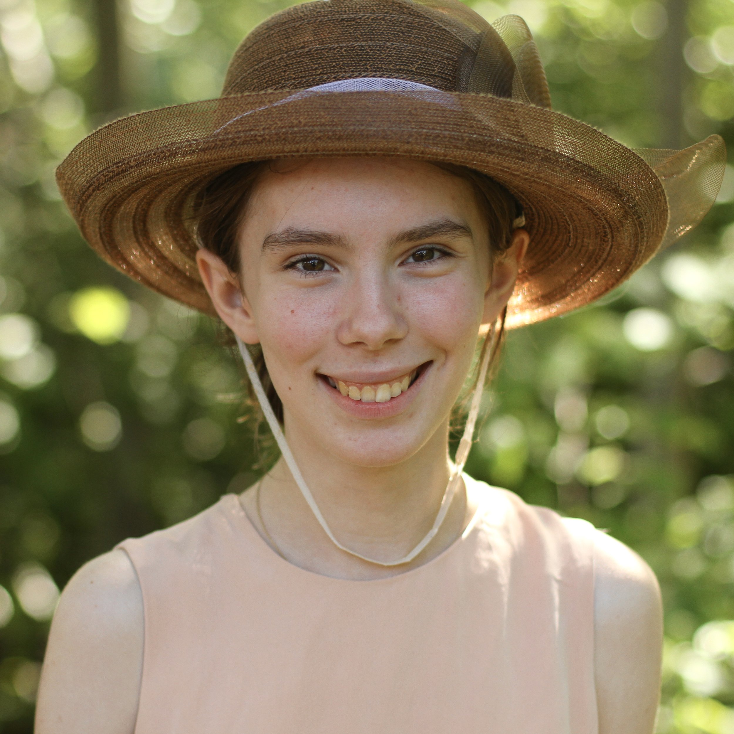 Smiling student with medium brown hair and straw hat