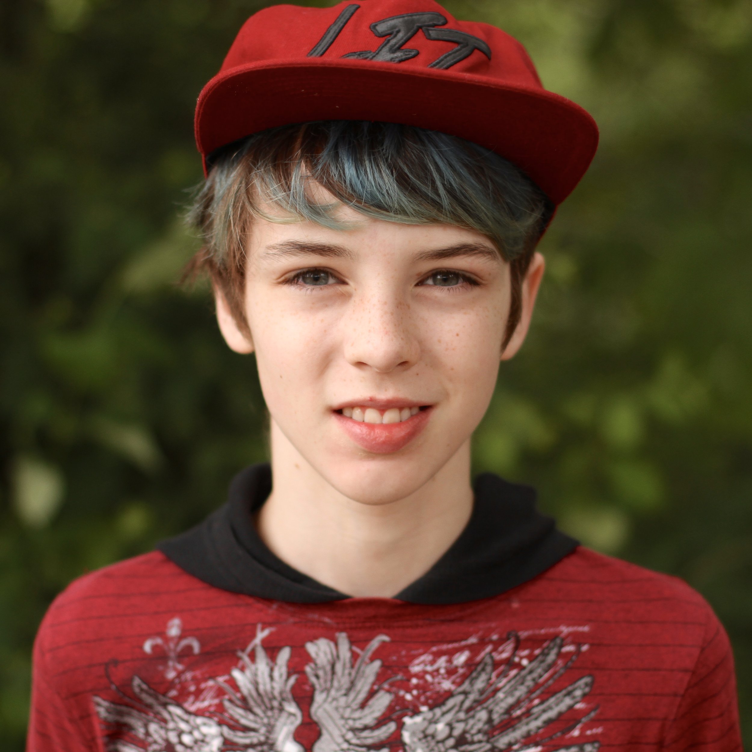 Smiling student with short blue hair and red baseball cap