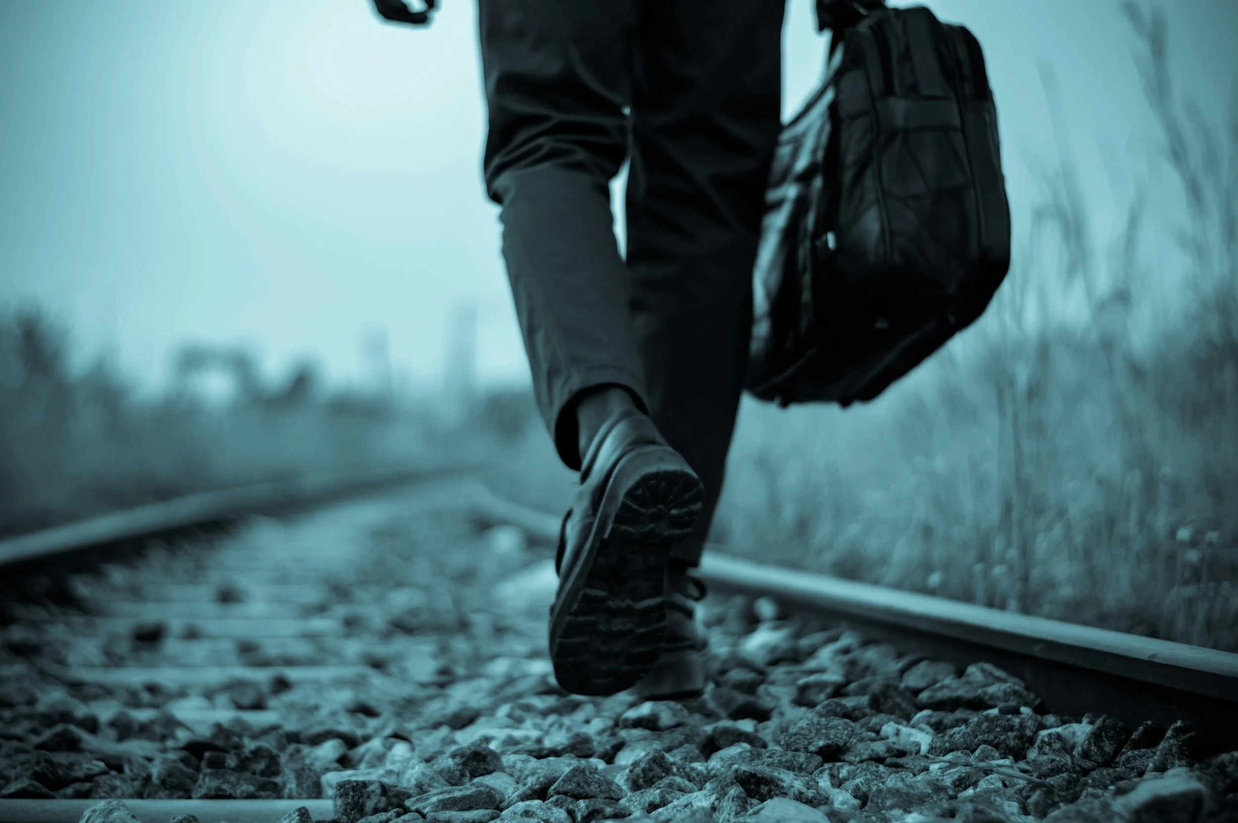 man with suitcase walking on tracks