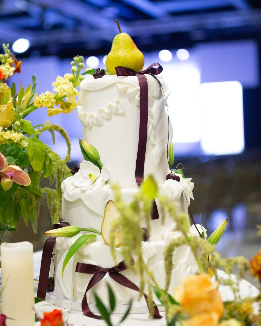 Trend alert 🍐🍒

We&rsquo;re seeing more and more couples choose fruit-forward cakes that blend modern styling with a natural twist&mdash;like this showstopper topped with a pear and adorned with burgundy ribbons, fresh florals, and cherries. It&rsq