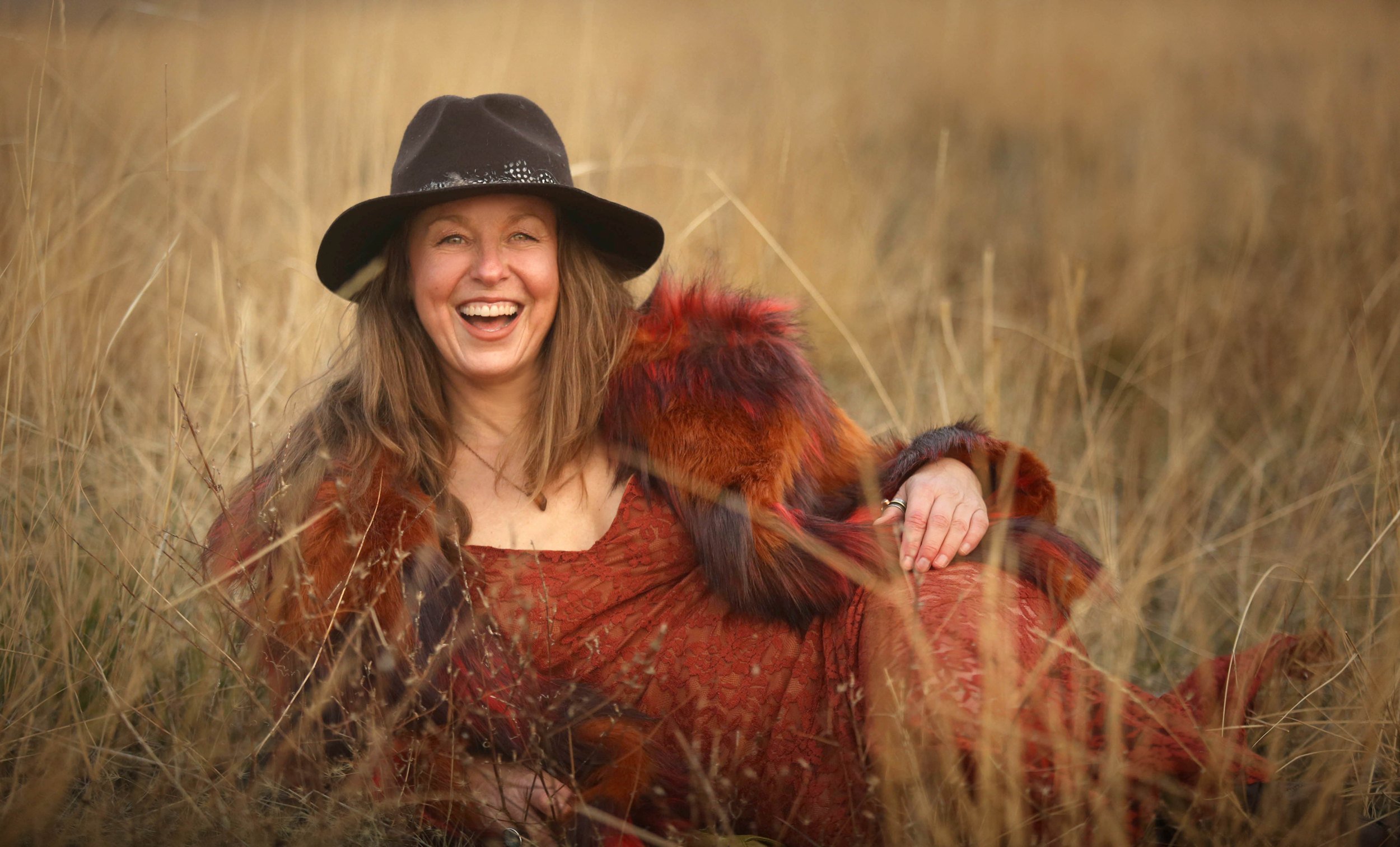 Kendra laughing in a fur jacket in a golden field