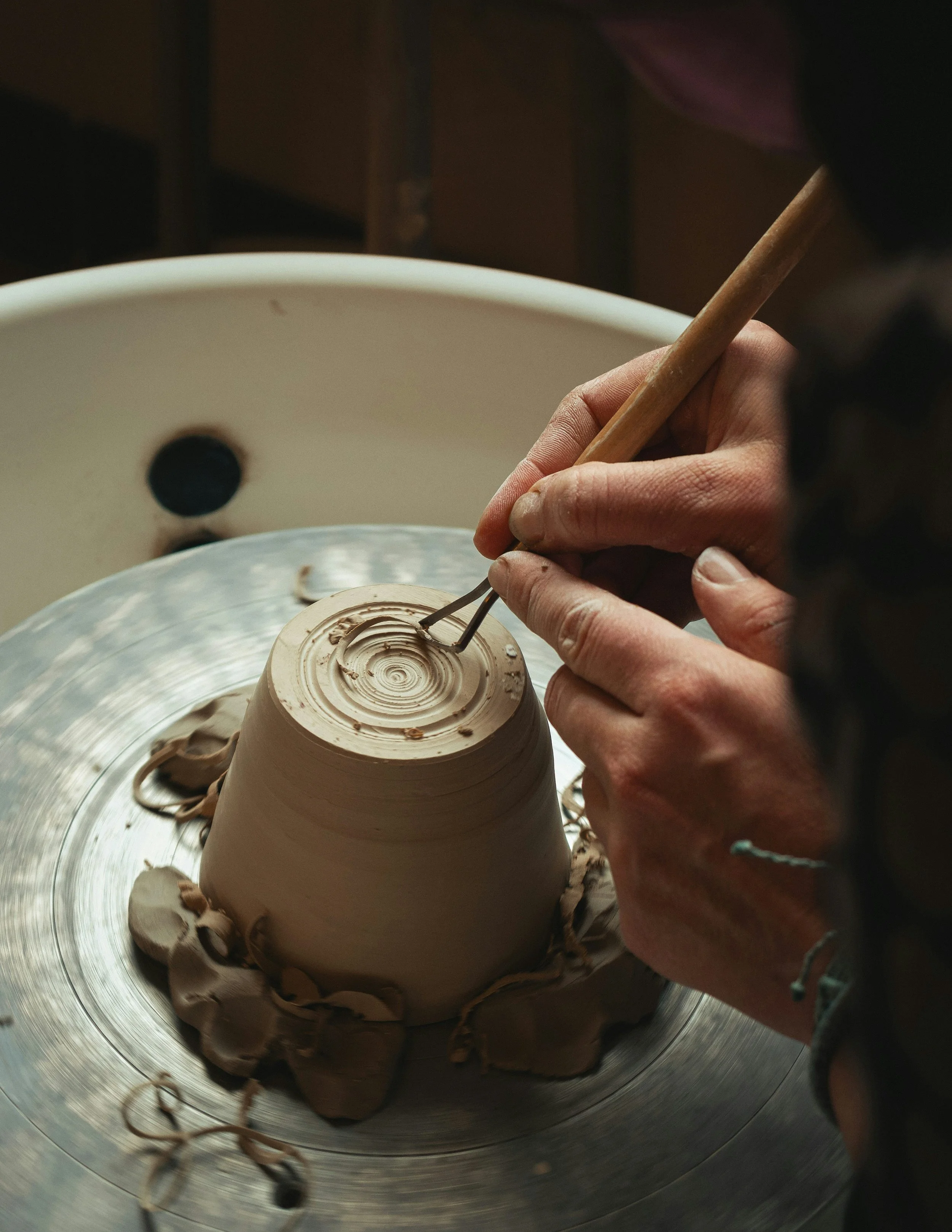 Close-up of hands shaping clay on a pottery wheel using small sculpting tools.