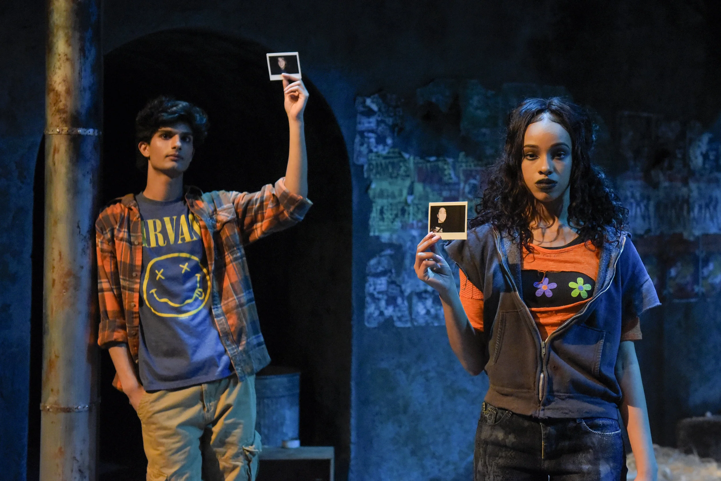 Orpheus (Yohana Ansari-Thomas) and an ensemble cast member (Farryl Lawon) hold up photographs of some of the real street youth whose interviews with playwright Naomi Iizuka inspired Polaroid Stories . Photo: Alessandra Mello.