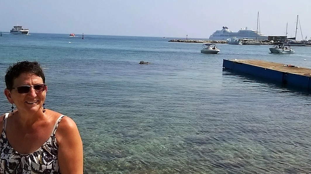 Francien in the historic harbour of Paphos. The harbour arm has a Roman breakwater sunk under the water. A cruiseship anchored offshore.