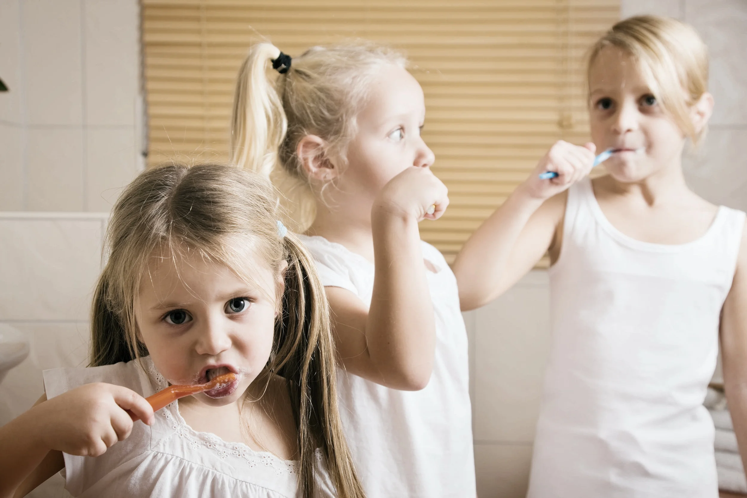 Three young girls brushing their teeth at home