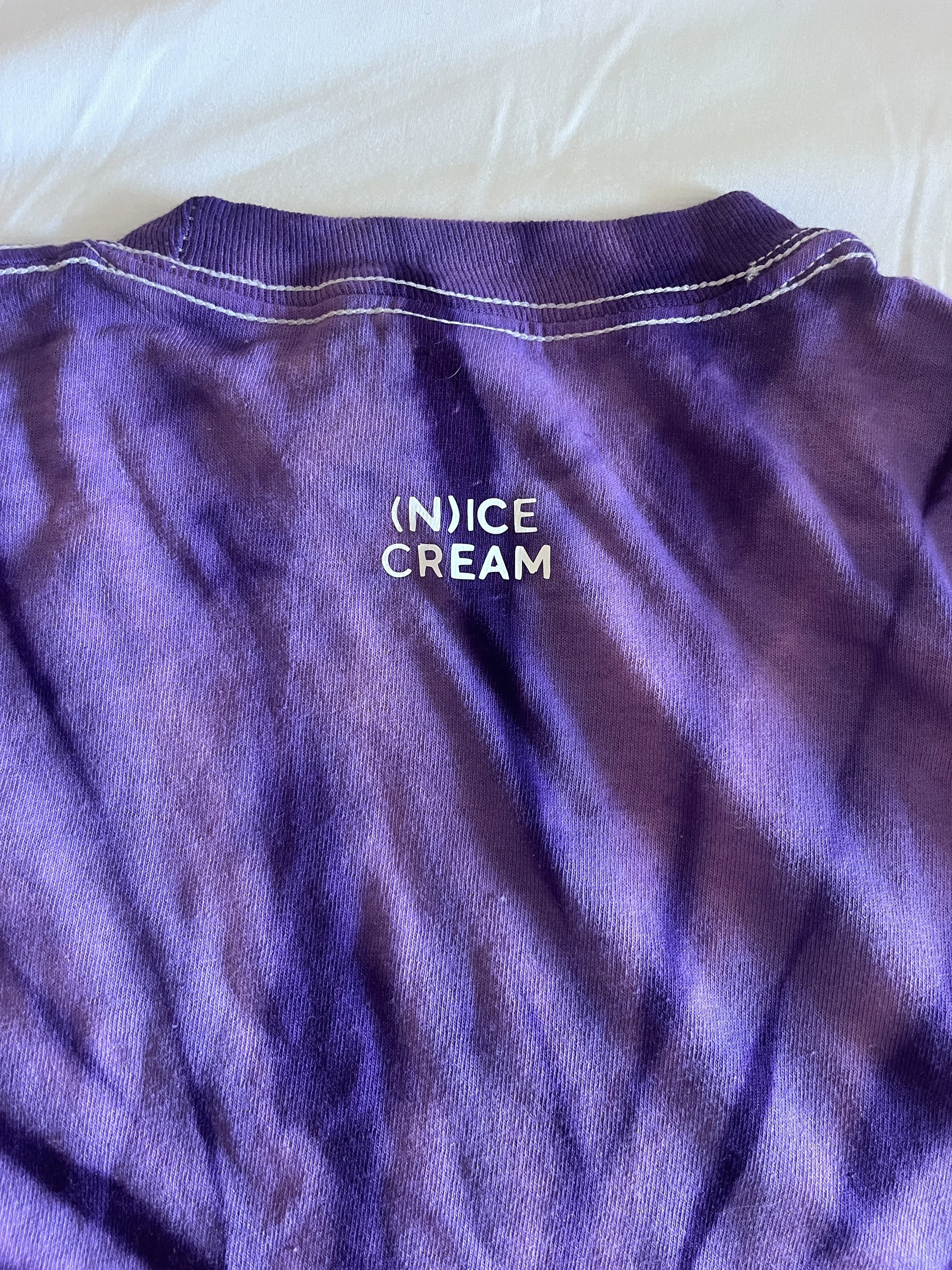 Close-up of a purple fabric shirt with white stitching and the text '(N)ICE CREAM' printed on it.