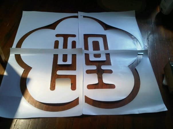 A large white sheet with a cut-out design of a logo featuring a stylized apple shape and a Korean character inside, placed on a wooden floor.