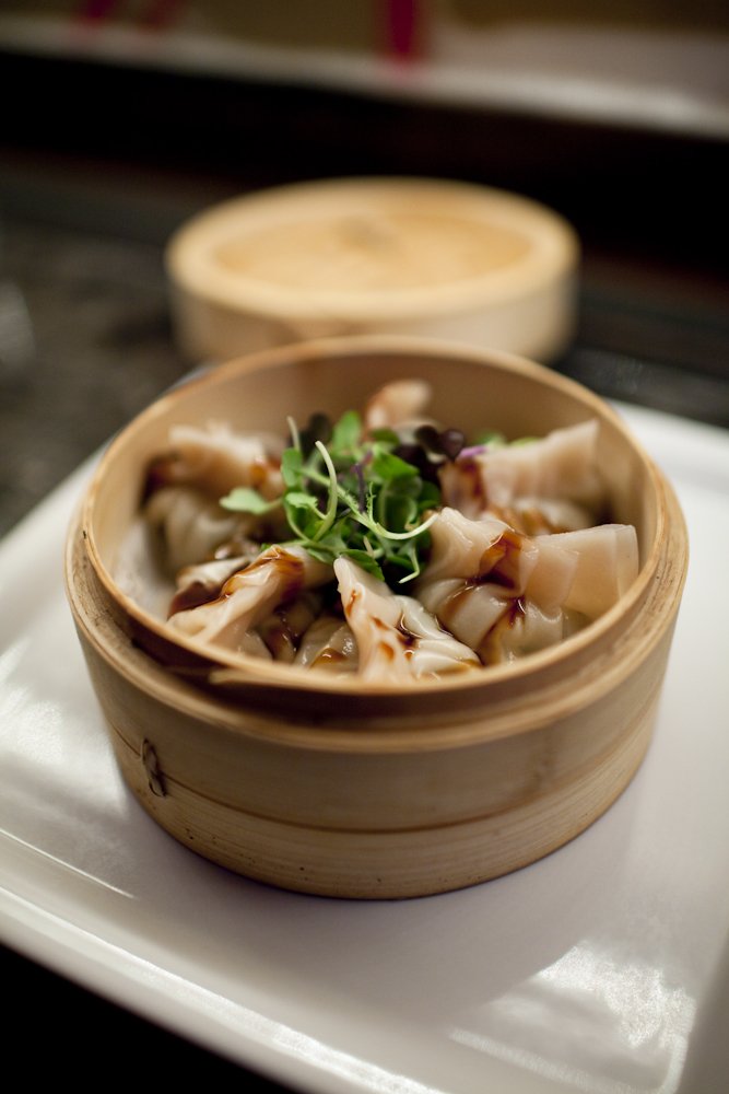 Dim sum dumplings served in a bamboo steamer basket, garnished with microgreens, on a white plate.
