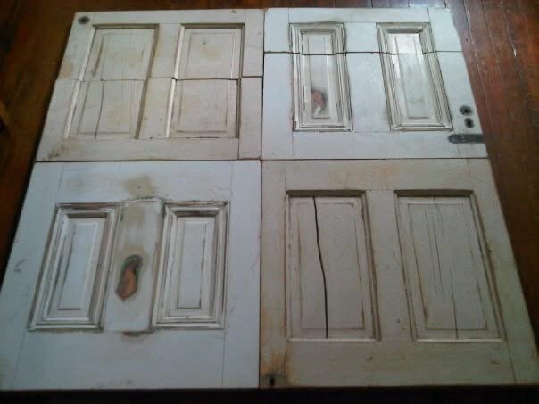 Four wooden cabinet doors laid flat on a wooden floor, showing different stages of sanding or refinishing.