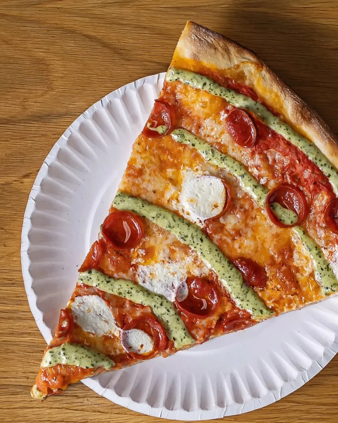 A slice of pizza with cherry tomatoes, cheese, and green sauce on a white paper plate.