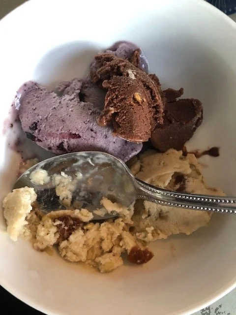 A bowl with four scoops of different flavors of ice cream and a metal spoon.