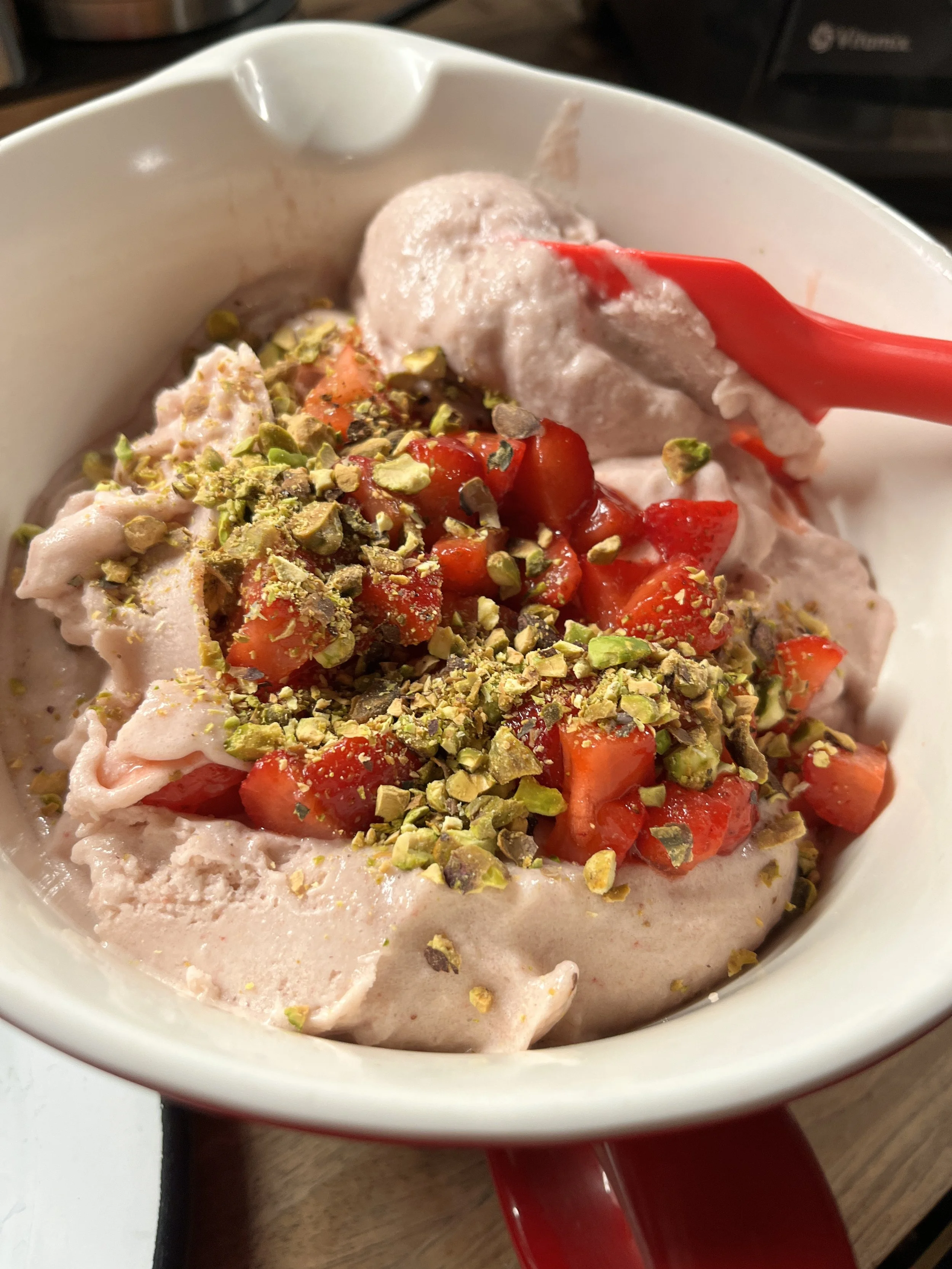 Frozen strawberry ice cream in a red mug topped with chopped pistachios and fresh strawberries.