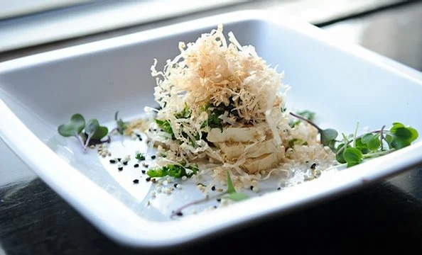 A plate of pasta topped with shredded cheese, garnished with microgreens and black sesame seeds.