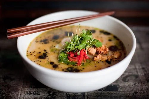A bowl of ramen with broth, green vegetables, pink pickled ginger, and black sesame seeds, with chopsticks on top.