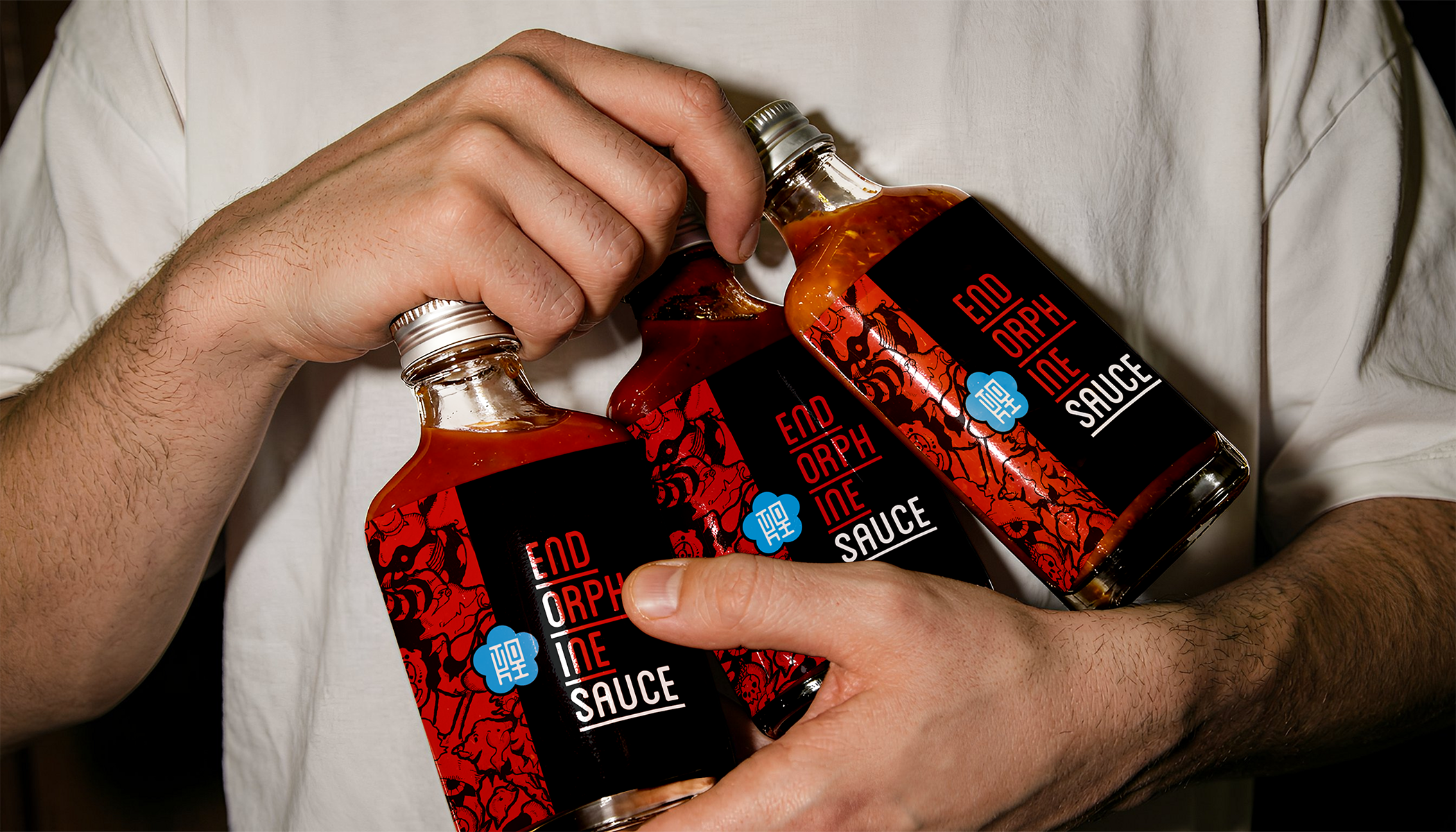 Person holding three bottles of hot sauce labeled 'Endorphin' against a plain background.