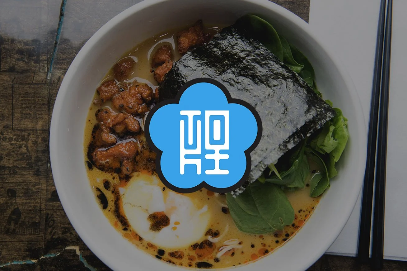 Bowl of ramen with seaweed, soft-boiled egg, green vegetables, and spicy meat topping on a wooden table.