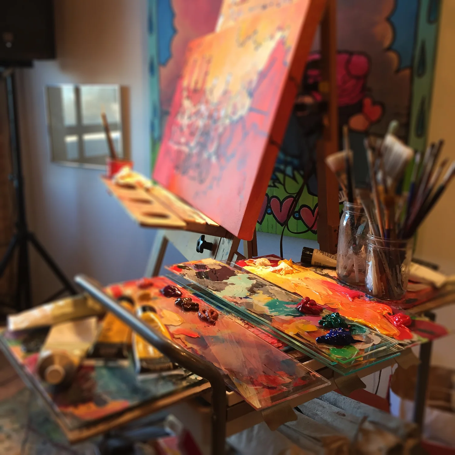 Studio view of Linnea's palette, paintbrushes, and colorful comm