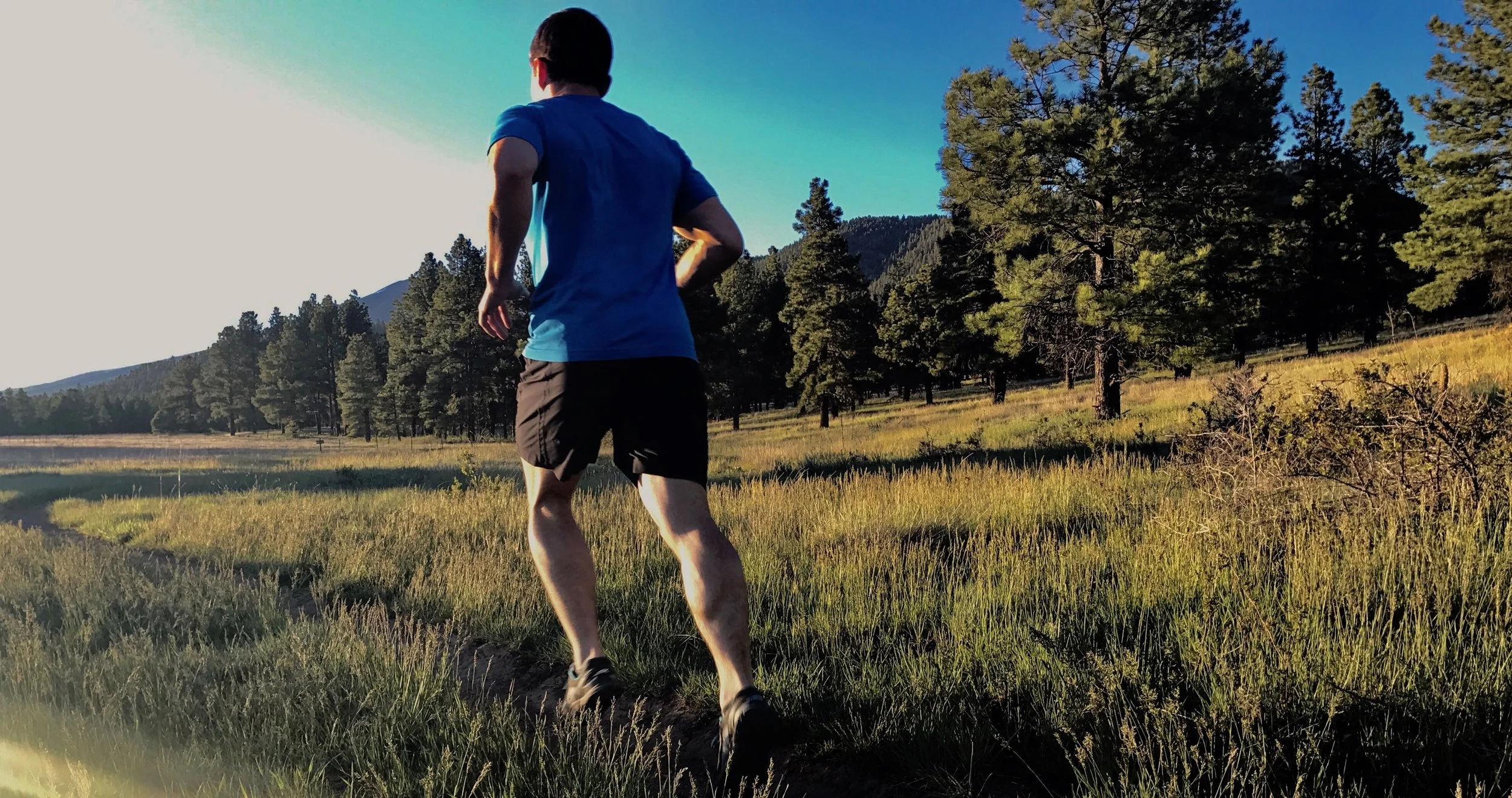 Photo of a man running at sunset with the Flagstaff mountains and forest in the background