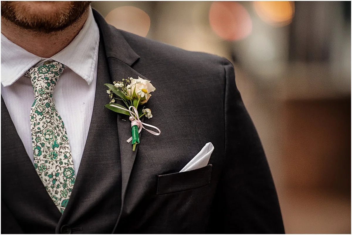 A closeup of the Groom's boutonniere with faded city lights behind him in Downtown Fredericksburg.