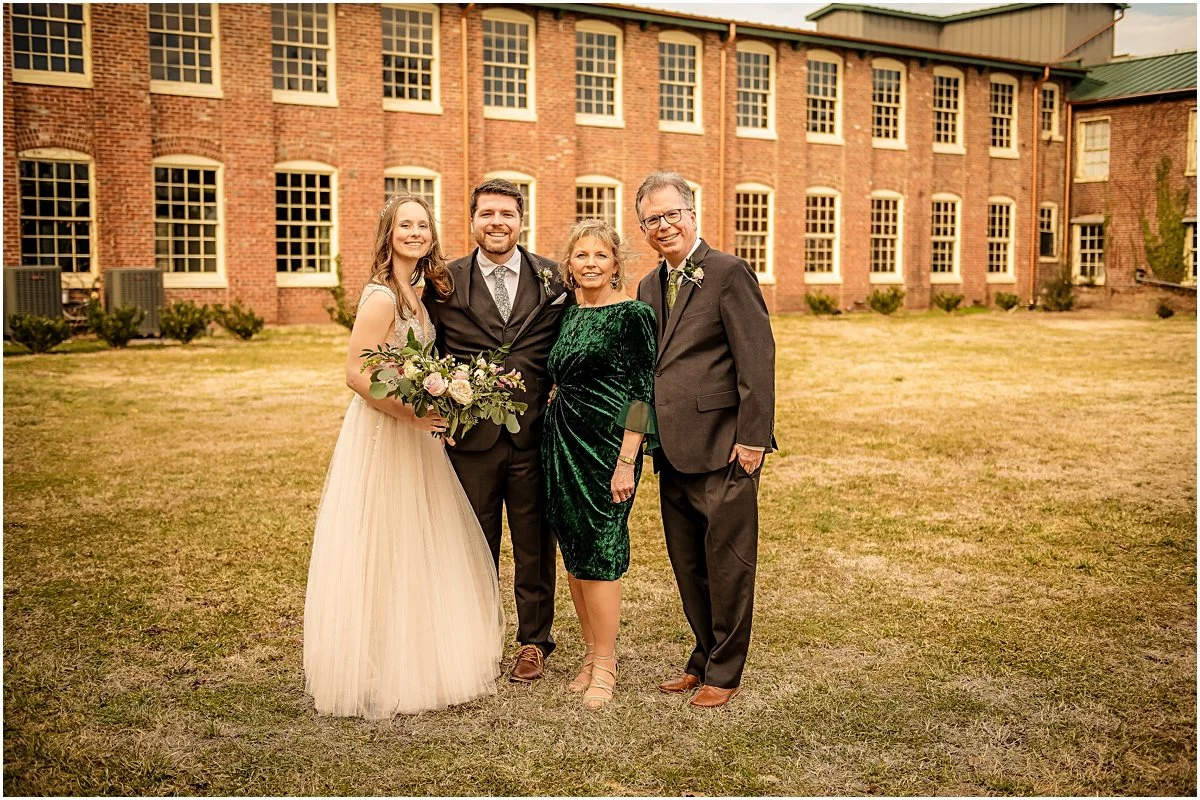 Colin and Sarah posing with his parents in front of a building during a wedding photography session in Downtown Fredericksburg.