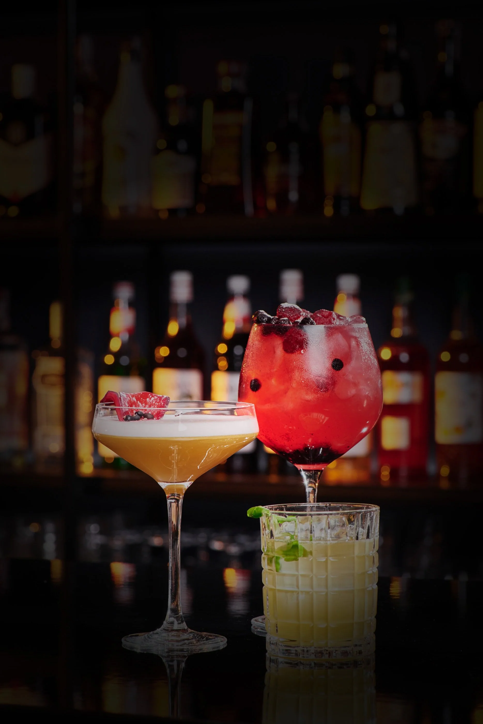 Trio of cocktails in front of shelves of liquor bottles.