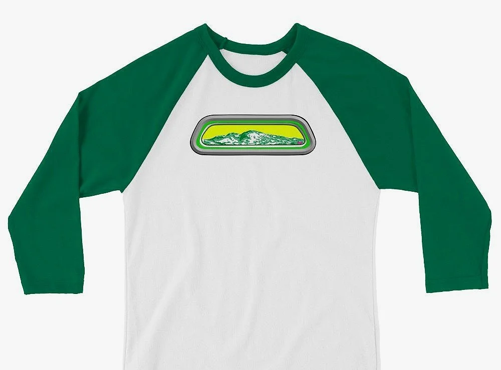 A white and green raglan-style shirt with a graphic of a mountain range viewed through a window on the front.