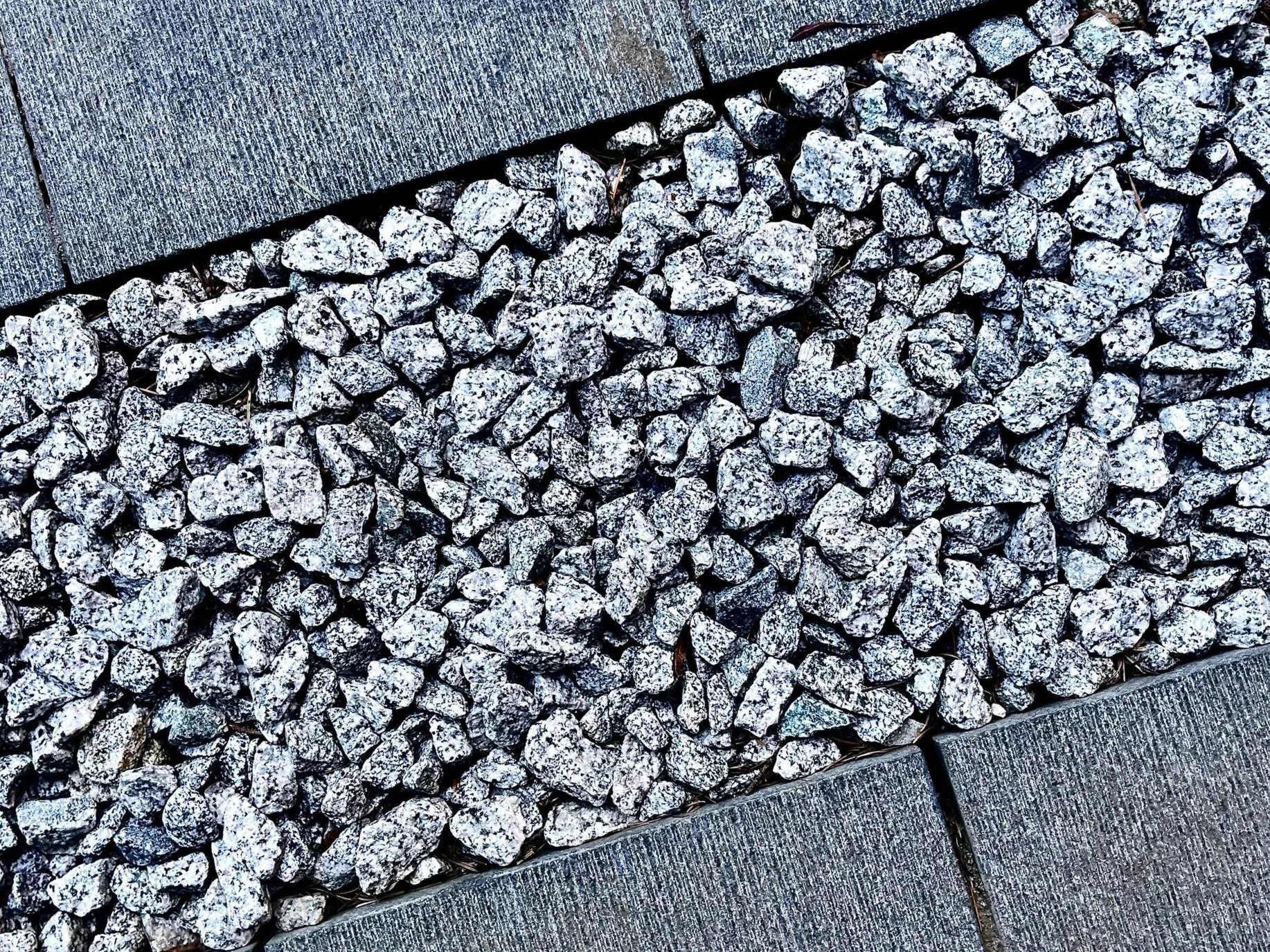 Close-up of gray gravel stones separated by dark grout lines between concrete paving slabs.