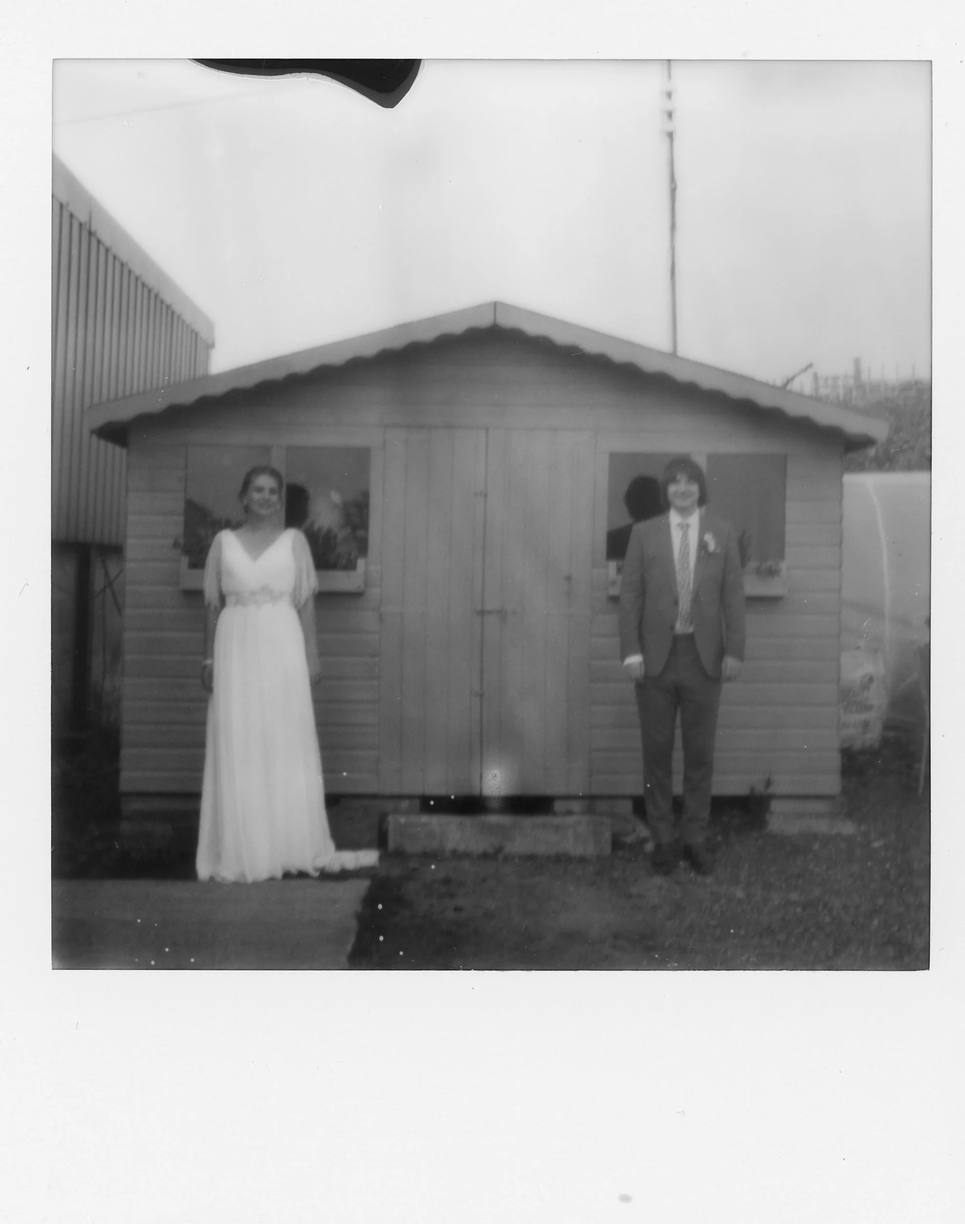 Instant black and white Polaroid photograph of Lucy and Marc at Well being Farm wedding Venue in Bolton. It is a Wes Anderson style Polaroid with Lucy and Marc stood at each window facing the camera straight on.