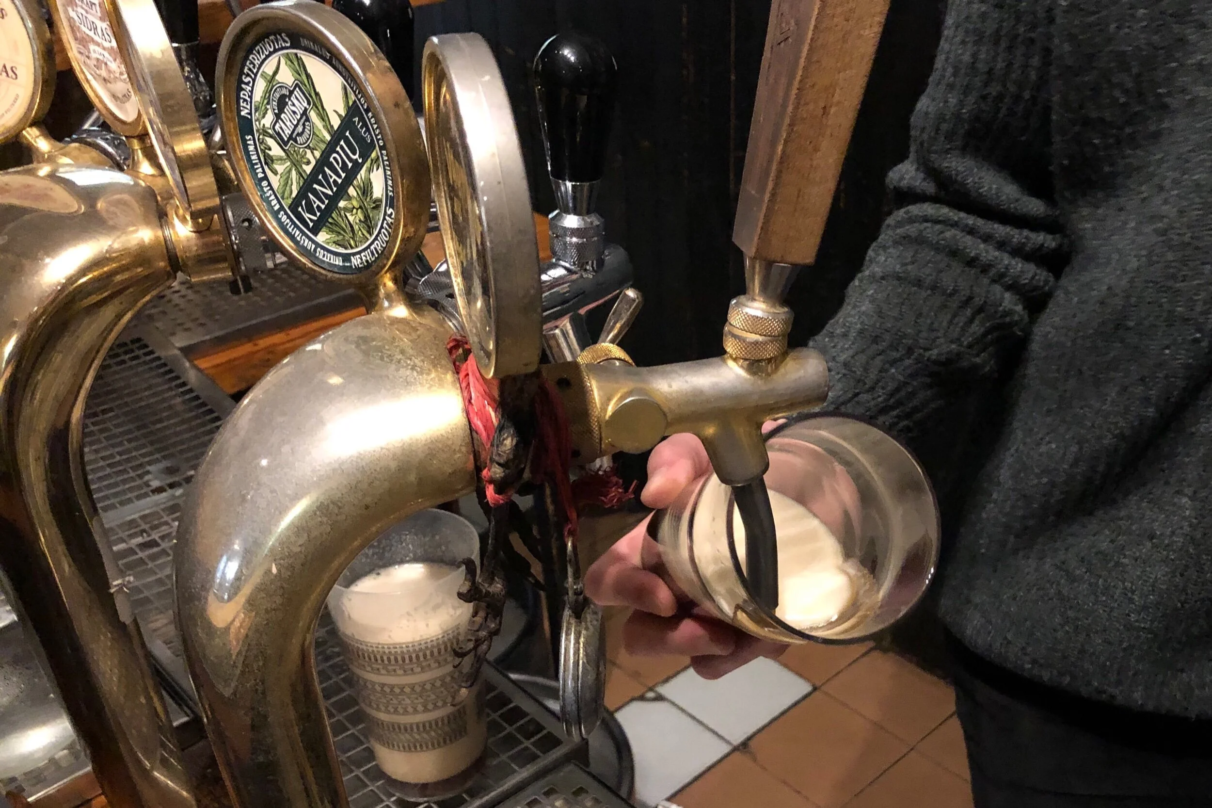 Pouring beer in Lithuania. Note the glass of foam and the little valve handle at the base of the tap. The flow of beer in this picture is more vigorous than is often the case.