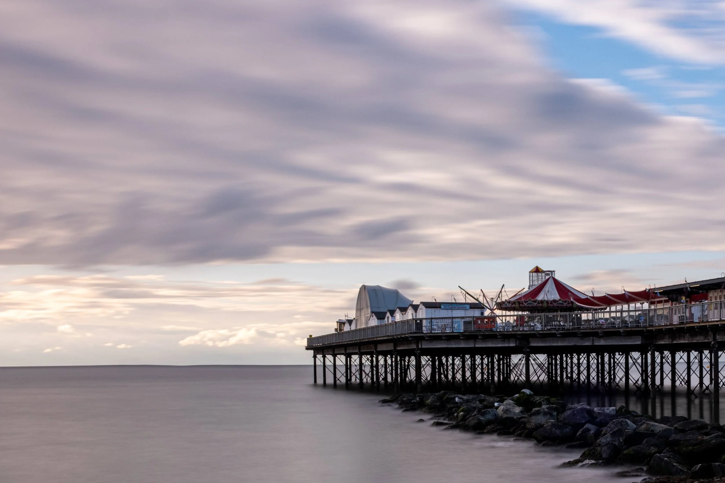 Pier extending over calm ocean under cloudy sky with a red and white striped tent on the pier.