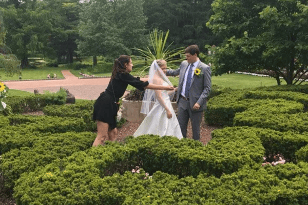 A wedding day dresser fixing the brides veil while the groom stares at her smiling