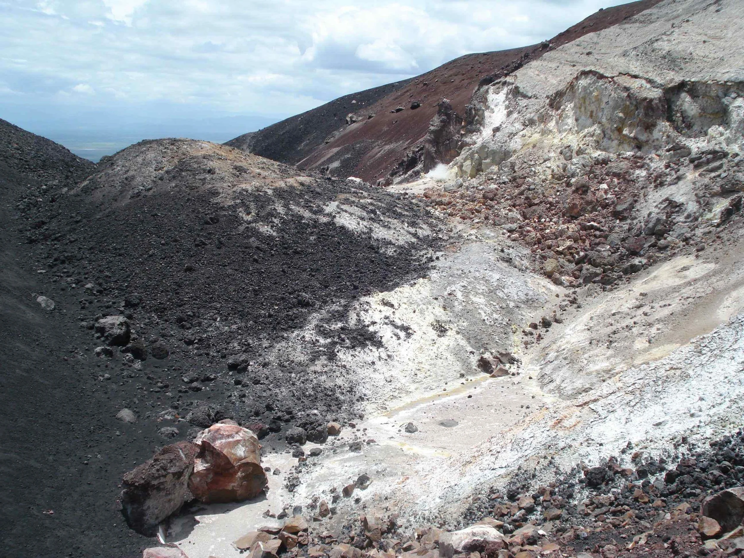 To the left is the fresh black basalt of the current cone. The light area on the right is the highly weathered inside flank of an older eruption cone. The flat middle area (pinkish) is an outwash basin or drainage area.