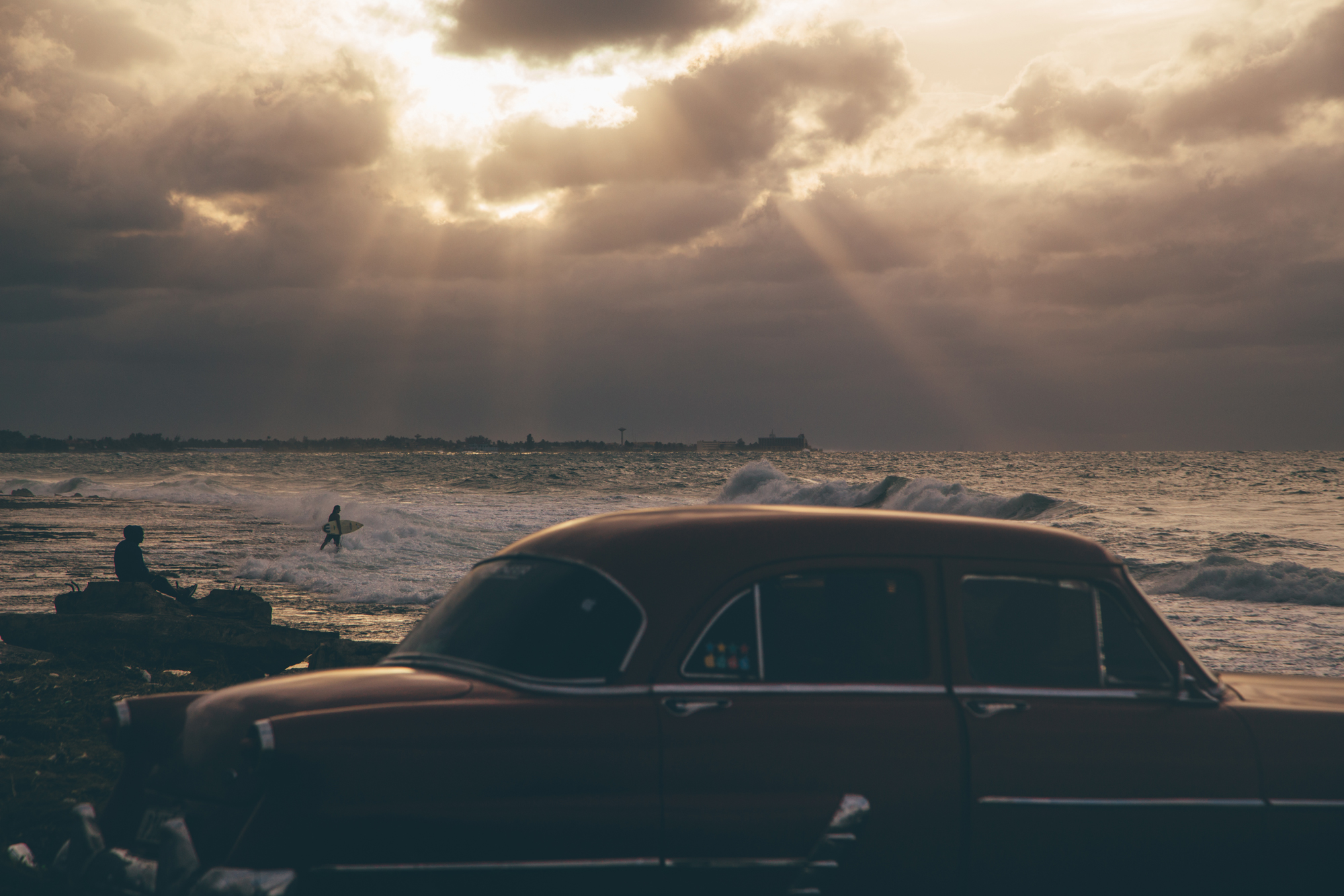 Surfers enter the water on a cloudy day along the treacherous Havana coast.