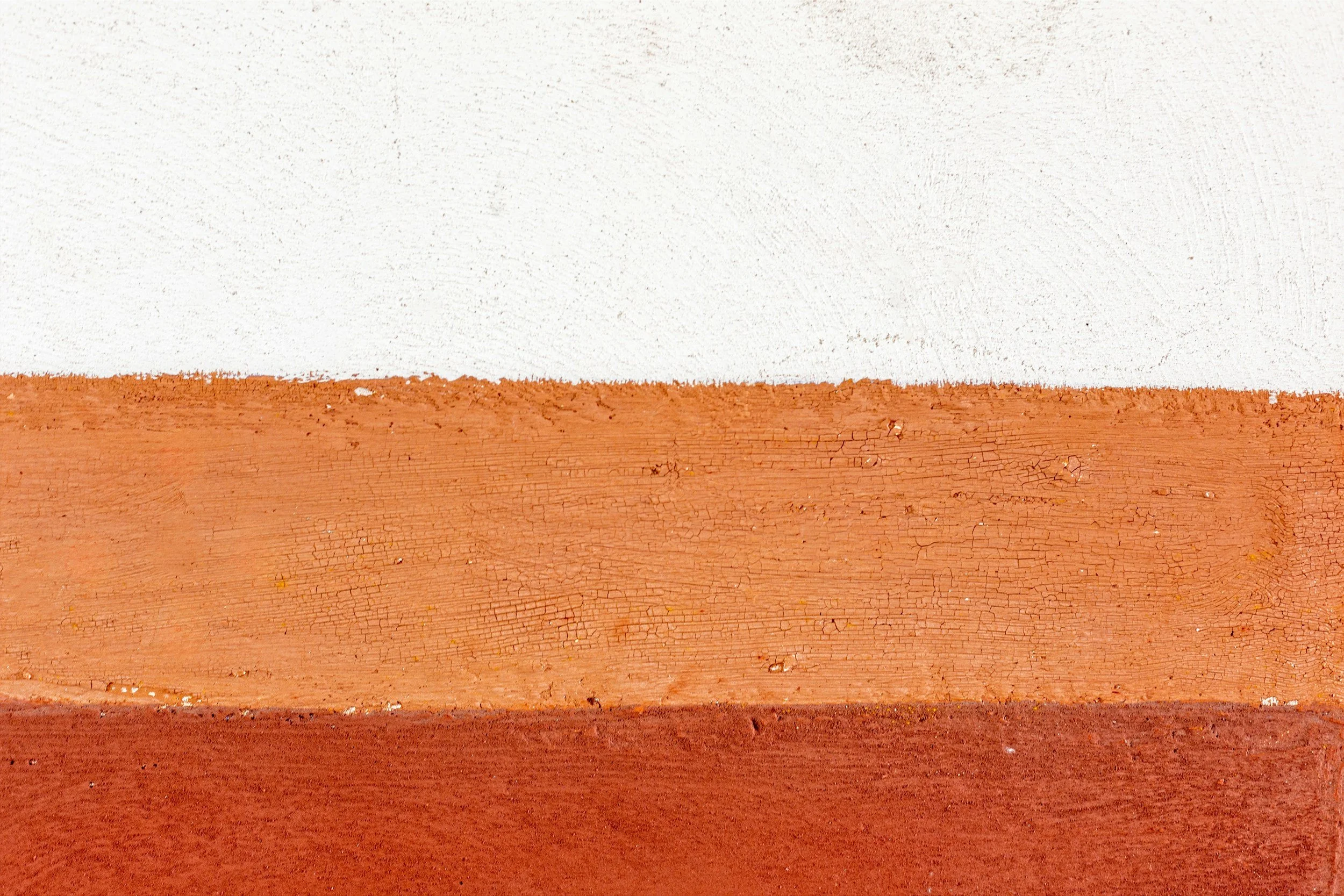 Close-up of a textured wooden surface painted in white, orange, and red horizontal stripes.