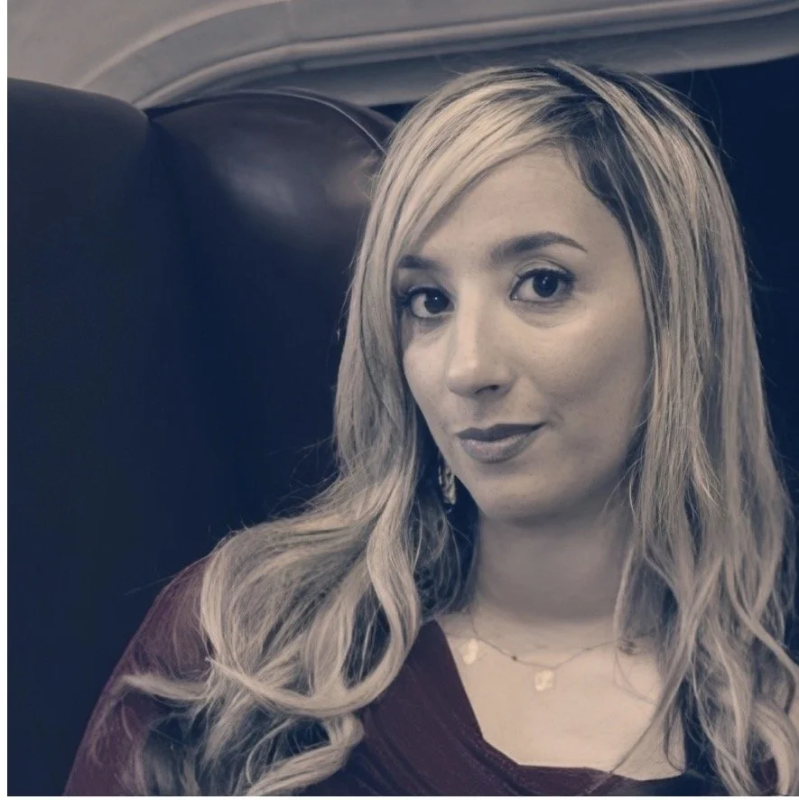 A woman with long blonde hair and a maroon top sitting in an airplane seat.