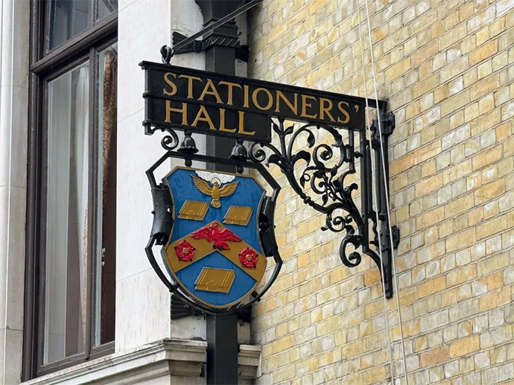 A-photo-of-the-Stationers'-Guild-coat-of-arms-on-the-outside-of-Stationers'-Hall-featuring-three-books-in-gold,-a-red-and-a-gold-dove,-and-two-red-rosettes.-Print-shop-West-Perth.