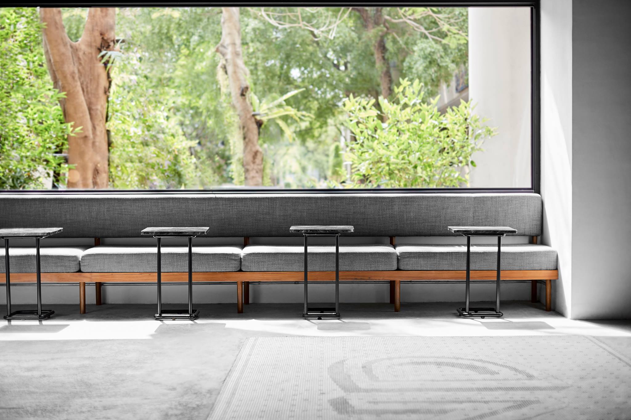 Our initial design brief was to create an inspiring coffee space that could facilitate learning environment as well as other various functions with the ultimate goal of bringing the university and coffee communities together. Working closely with faculties on campus, Blend café aspires to become a communal space for students, a stage where they can fully express their individuality, talents and learn more about specialty coffee. The space is located in one of the busiest common area on ground floor in one of the main lecture building (Building 6) on Dhurakij Pundit University. With limited space of 100 sqm, the ultimate challenge was to incorporate different functions such as art gallery, exhibition, coffee workshop, competition & class and other private events into a coffee space without sacrificing specialty coffee bar look, vibe and feel. This multi-purpose space requirement was achieved through our innovative approach of reinventing the main centered long table with a pulley mechanic function. Working closely with our engineering team, the centered table can be adjusted to three different height levels above the floor; 75 cm to serve as coffee retail function, 120 cm to serve as art exhibition & gallery space and the ceiling height to create a standing room atmosphere, where loose furniture can fill-up the space depending on a diverse function requirement. Constructing an iconic view for the main coffee bar was our other focus. The bar view must be able to attract attention as well as delivering an inviting atmosphere for customer-barista interaction. Coffee enthusiasts and customers would be able to engage and observe coffee craftmanship up-close with our “Open bar minimalistic design”. From the position of the espresso machine placed in alignment with the back-entrance access point to drip station layout have been considered thoroughly to further enhance customer coffee drinking experience. The final design has successfully merged multi-functional spaces into a singular “Convertible” café space, breaking free from an old fashioned café design concept. The centered mechanic table that can be retracted fully upright to ceiling height offers a spacious area for hosting assorted events and functions. An “Oversized steel glass accordion door” is another core element that enables the space to overcome its 100 sqm limitation, connecting the café space to the outside community area when it’s fully opened. This freedom also allows the café to accommodate weather and season change accordingly, transforming its topology from an outdoor, semi-outdoor to an enclosed coffee space. Over the past year, Blend café has successfully launched coffee classes, drip coffee competition, cupping events, exhibition, gallery and workshops to coffee enthusiasts, students, university staff, blending in the communities altogether. The team hope this forward-thinking approach would continue to inspire creativity and innovation among students, designers through to younger generation in Thailand.