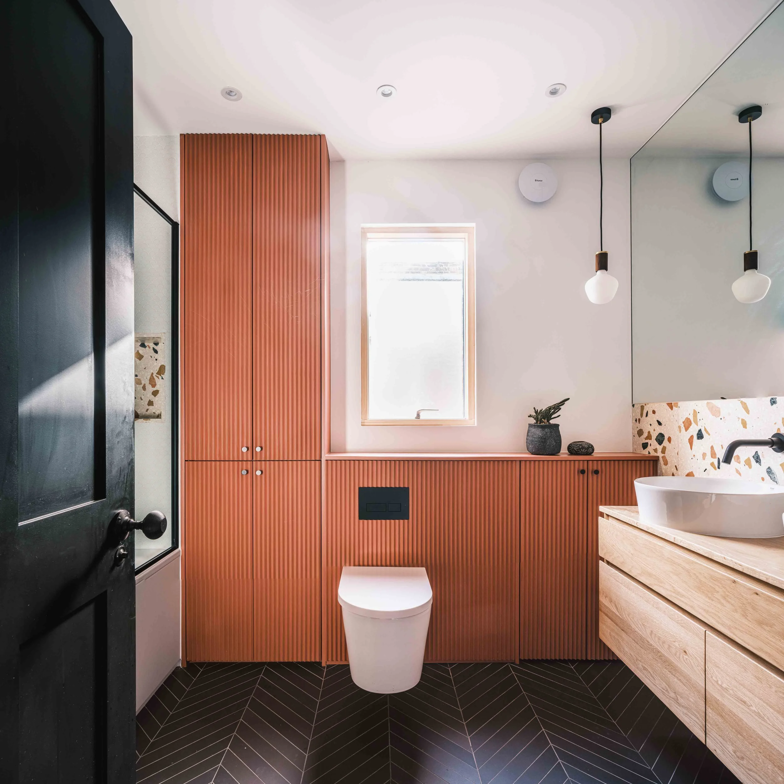 Bathroom with fluted terracotta joinery and black tiled floor 