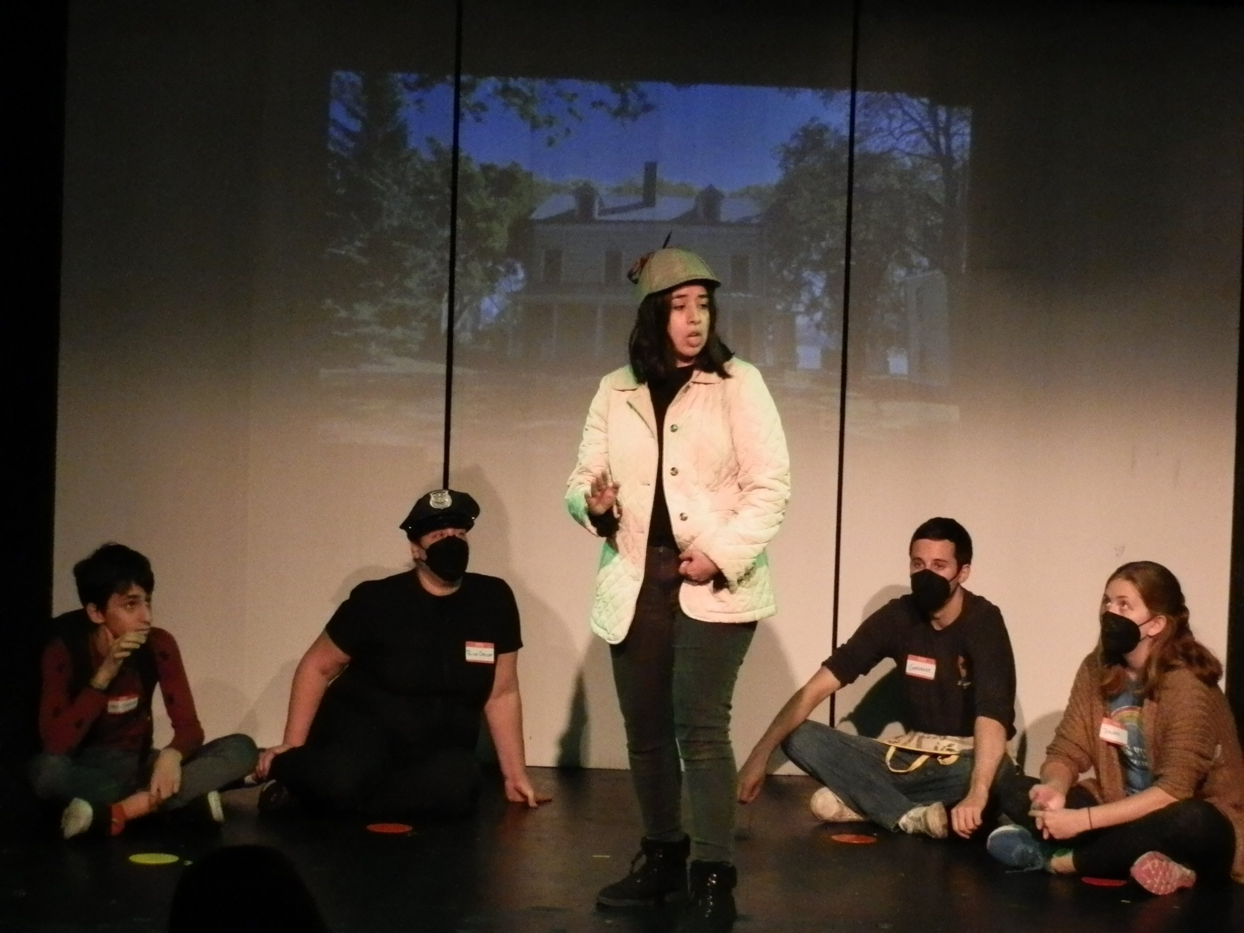  Lluvia Almanza as Detective Sharpe with an audience of suspects in  The Mystery of the Green Teeth Ghost.  Photo by Robert René Galván. 