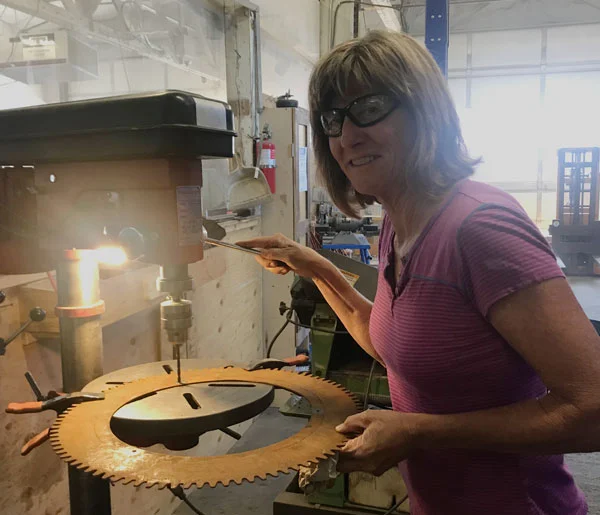 Rochelle @ DIY Cave using the drill press drilling holes in our gear. We plan to mechanically affix the largest metal components to the wall, in addition to mortaring the mosaic panels in place.