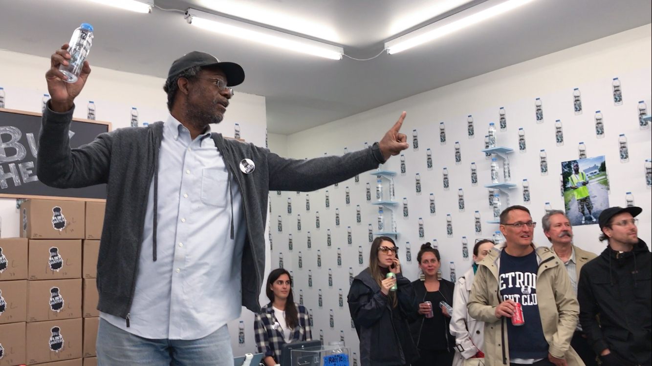 Pope.L auctions a bottle of Flint Water signed by the artist during the opening of Flint Water, September 7, 2017 at What Pipeline, Detroit. Courtesy the Artist and What Pipeline. © Pope.L Homepage image: Pope.L, Flint Water Single Unsigned Bottle , 2017. 16 oz. plastic bottle of contaminated water obtained from Flint, MI. Courtesy the artist and What Pipeline. © Pope.L