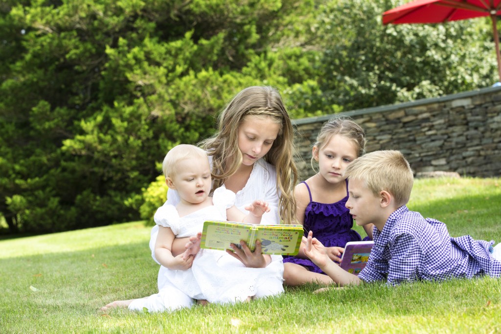  Siblings reading a book to their younger sister at their home photo shoot 